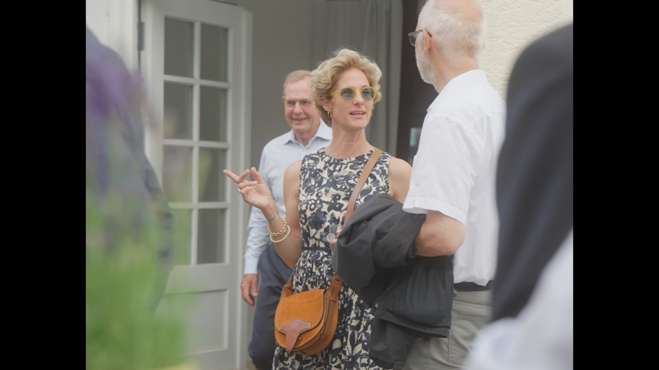 Das Bild steht in Zusammenhang mit Mediation und Konfliktlösung durch die Kanzlei Ponschab & Partner und zeigt folgendes: Eine Frau in einem ärmellosen gemusterten Kleid und mit Sonnenbrille gestikuliert im Gespräch mit einem Mann in einem weißen Hemd. Ein weiterer Mann steht im Hintergrund neben einer offenen Tür. Die Szene scheint im Freien in der Nähe eines Gebäudes zu spielen. Bei Fragen zu Konflikten und Konfliktlösung wenden Sie sich bitte an uns unter info@ponschab-partner.com