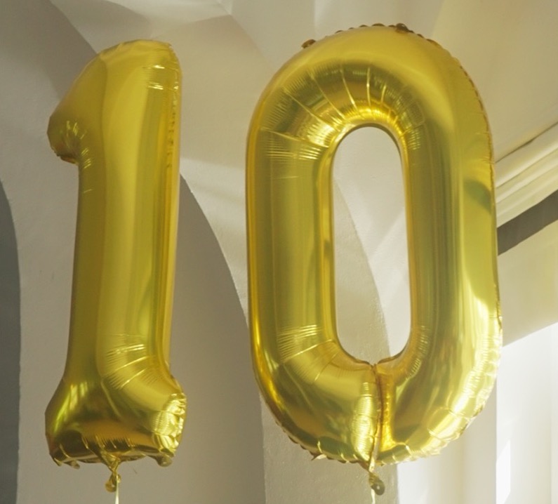 Das Bild steht in Zusammenhang mit Mediation und Konfliktlösung durch die Kanzlei Ponschab & Partner und zeigt folgendes: Zwei große goldene Folienballons, die wie die Zahlen 1 und 0 geformt sind, schweben in einem Raum und bilden zusammen die Zahl 10. Bei Fragen zu Konflikten und Konfliktlösung wenden Sie sich bitte an uns unter info@ponschab-partner.com