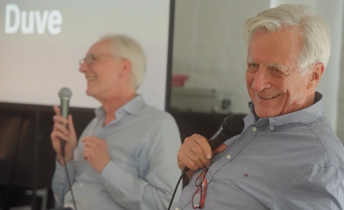 Das Bild steht in Zusammenhang mit Mediation und Konfliktlösung durch die Kanzlei Ponschab & Partner und zeigt folgendes: Zwei ältere Männer mit grauem Haar sitzen in einem Haus, jeder hält ein Mikrofon und lächelt. Ein Mann erscheint scharf im Vordergrund, während der andere unscharf im Hintergrund in der Nähe eines Bildschirms zu sehen ist, auf dem ein Teil des Textes angezeigt wird. Bei Fragen zu Konflikten und Konfliktlösung wenden Sie sich bitte an uns unter info@ponschab-partner.com