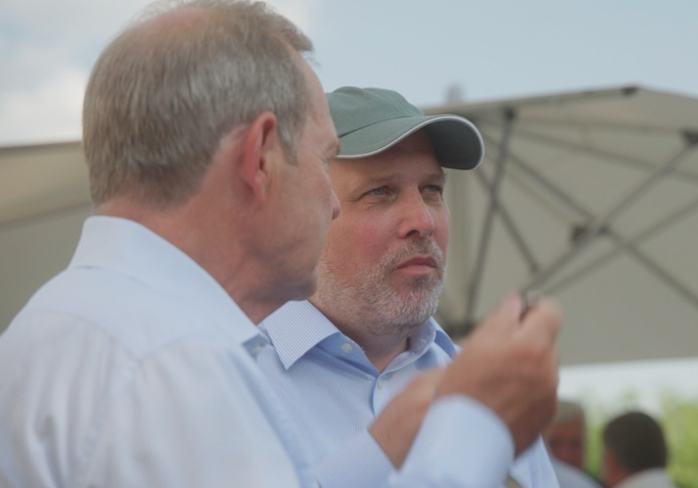 Das Bild steht in Zusammenhang mit Mediation und Konfliktlösung durch die Kanzlei Ponschab & Partner und zeigt folgendes: Zwei Männer stehen im Freien vor einem großen Regenschirm. Ein Mann blickt von der Kamera weg, während der andere, der eine grüne Mütze und ein blaues Hemd trägt, nach vorne schaut. Beide scheinen in ein Gespräch vertieft zu sein. Bei Fragen zu Konflikten und Konfliktlösung wenden Sie sich bitte an uns unter info@ponschab-partner.com