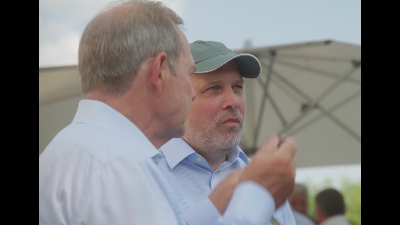 Das Bild steht in Zusammenhang mit Mediation und Konfliktlösung durch die Kanzlei Ponschab & Partner und zeigt folgendes: Zwei Männer in hellen Hemden stehen im Freien, der eine schaut von der Kamera weg, der andere trägt eine graue Mütze und blickt nach vorne. Im Hintergrund ist ein offener Regenschirm zu sehen. Bei Fragen zu Konflikten und Konfliktlösung wenden Sie sich bitte an uns unter info@ponschab-partner.com