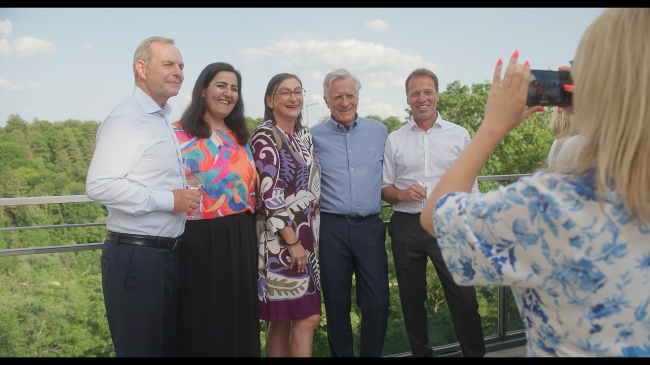 Das Bild steht in Zusammenhang mit Mediation und Konfliktlösung durch die Kanzlei Ponschab & Partner und zeigt folgendes: Fünf Personen stehen in einer Reihe und posieren für ein Foto auf einem Außenbalkon mit Grünpflanzen im Hintergrund. Eine sechste Person im Vordergrund macht ihr Foto mit einem Smartphone. Die Gruppe ist in legerer Business-Kleidung gekleidet. Bei Fragen zu Konflikten und Konfliktlösung wenden Sie sich bitte an uns unter info@ponschab-partner.com