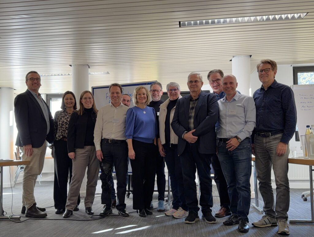 Das Bild steht in Zusammenhang mit Mediation und Konfliktlösung durch die Kanzlei Ponschab & Partner und zeigt folgendes: Eine Gruppe von elf Erwachsenen steht drinnen in einem gut beleuchteten Konferenzraum zusammen. Sie sind in legerer Business-Kleidung gekleidet und lächeln in die Kamera. Im Hintergrund sind Tische, Stühle und ein Flipchart zu sehen. Bei Fragen zu Konflikten und Konfliktlösung wenden Sie sich bitte an uns unter info@ponschab-partner.com